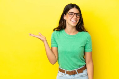 Sarı arka planda izole edilmiş genç beyaz kadın bir ilan vermek için avucunun içinde hayali bir mekan tutuyor.