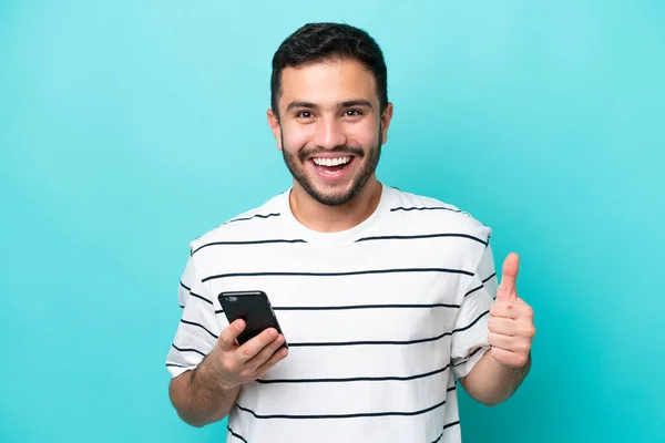 Jovem Brasileiro Isolado Fundo Azul Usando Telefone Celular Enquanto Faz — Fotografia de Stock