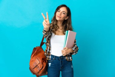 Mavi arka planda izole genç bayan gülümseyerek ve zafer işareti göstererek