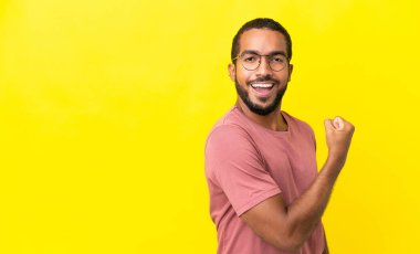 Sarı arka planda izole edilmiş genç latin adam güçlü hareketler yapıyor.