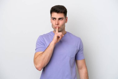 Beyaz arka planda izole edilmiş genç beyaz bir adam sessizlik işareti gösteriyor. Parmağını ağzına sokuyor.
