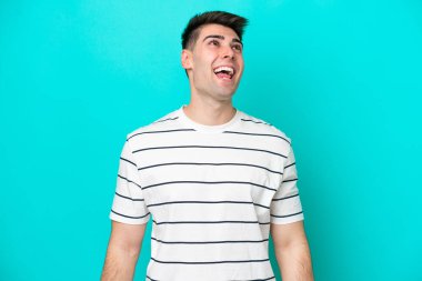 Kafkasyalı genç adam mavi arka planda tek başına gülüyor.