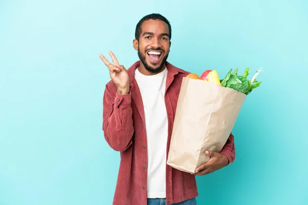 Joven Latino Sosteniendo Una Bolsa Compras Aislada Sobre Fondo Azul —  Fotos de Stock