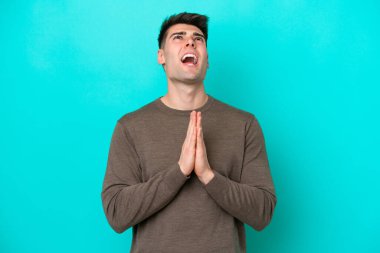 Mavi arka planda izole edilmiş genç beyaz adam avuç içlerini bir arada tutuyor. İnsan bir şey ister.