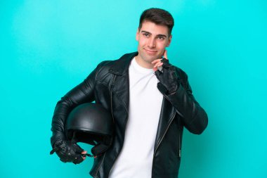 Motosiklet kasklı genç beyaz adam mavi arka planda izole edilmiş. Şüpheleri var.