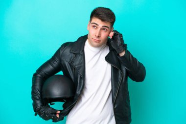 Motosiklet kasklı genç beyaz adam mavi arka planda izole edilmiş hayal kırıklığına uğramış ve kulaklarını kapatmış.