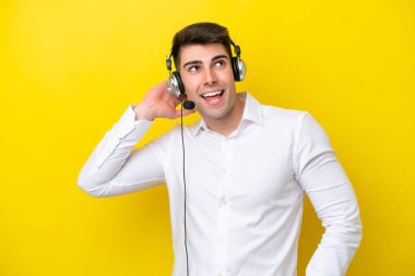 Tele pazarlamacı beyaz adam sarı arka planda izole edilmiş bir kulaklıkla çalışıyor.