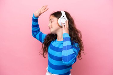 Küçük kız pembe arka planda izole edilmiş müzik ve dans dinliyor.