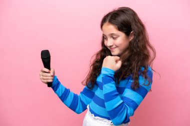 Pembe arka planda izole edilmiş bir mikrofonu kaldıran küçük şarkıcı kız zaferi kutluyor.