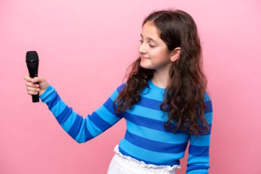 Küçük şarkıcı kız pembe arka planda izole edilmiş neşeli bir mikrofonu kaldırıyor.