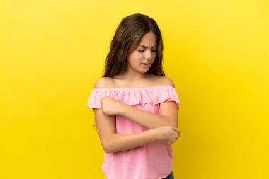 Küçük beyaz kız, sarı arka planda izole edilmiş, dirseğinde ağrı var.