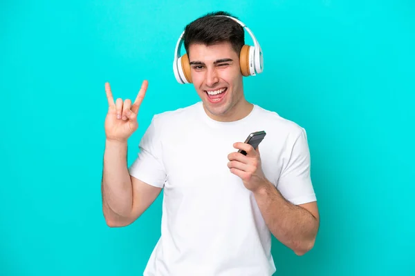 Jovem Caucasiano Isolado Fundo Azul Ouvindo Música Com Gesto Rock — Fotografia de Stock
