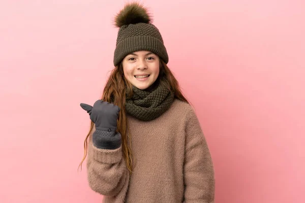 모자를 분홍색 배경에 고립된 소녀가 제품을 제공하는 측면을 가리키고 — 스톡 사진