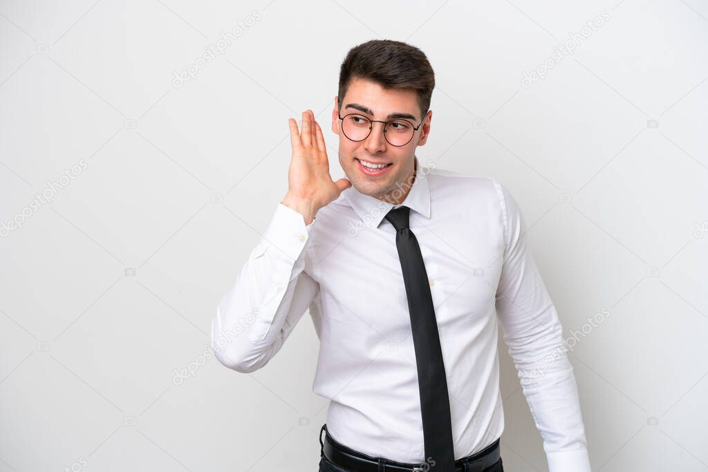 Business caucasian man isolated on white background listening to something by putting hand on the ear