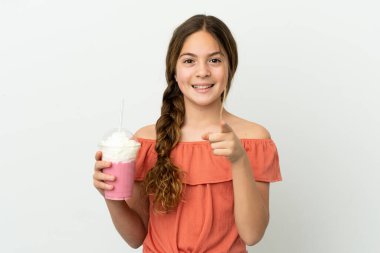 Beyaz arka planda izole edilmiş çilekli milkshake ile küçük beyaz kız şaşırmış ve ön tarafı işaret ediyor.
