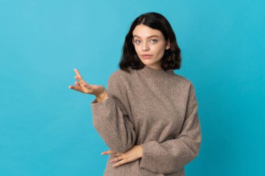 Genç Ukraynalı kız mavi arka planda izole edilmiş, kuşkuları var.