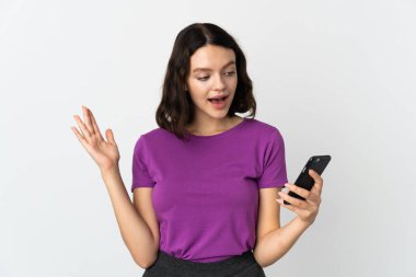 Genç Ukraynalı kız beyaz arka planda izole edilmiş kameraya bakarken şaşırmış bir ifadeyle cep telefonunu kullanıyor.