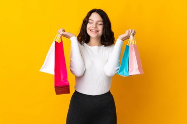 Ukraynalı genç bir kız sarı arka planda izole edilmiş alışveriş torbaları tutuyor ve gülümsüyor.