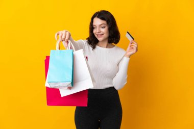 Ukraynalı genç bir kız sarı arka planda izole edilmiş. Elinde alışveriş çantaları ve bir kredi kartı var.