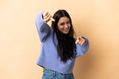 İzole edilmiş arka planda genç beyaz kadın mutlu bir ifadeyle ön tarafı işaret ediyor