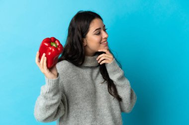 Mavi arka planda karabiber tutan beyaz bir kadın bir fikir üretiyor ve ona bakıyor.
