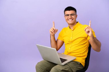 Genç adam dizüstü bilgisayarla bir sandalyede oturmuş harika bir fikri işaret ediyor.