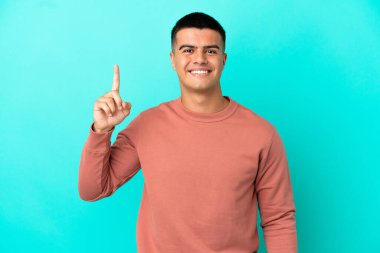 Soyutlanmış mavi arka planı olan yakışıklı genç adam harika bir fikre işaret ediyor.