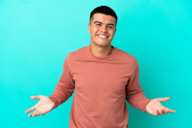 Soyutlanmış mavi arka planda genç yakışıklı adam mutlu ve gülümsüyor.