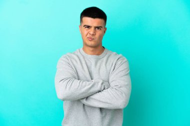 Mutsuz bir ifadeyle soyutlanmış mavi arka planı olan genç yakışıklı bir adam.
