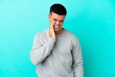 Genç, yakışıklı, soyutlanmış, mavi arka planlı, diş ağrısı olan bir adam.