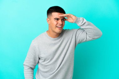 Soyutlanmış mavi arka planda genç yakışıklı bir şey aramak için çok uzaklara bakıyor.