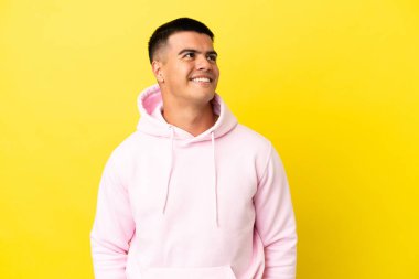 Soyutlanmış sarı arka planda genç yakışıklı bir adam yukarı bakarken bir fikir düşünüyor.