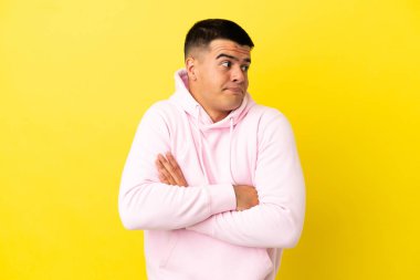 Izole sarı arka plan üzerinde genç yakışıklı adam omuzları kaldırırken şüphe jest yapma