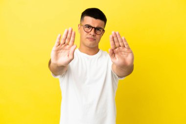 Soyutlanmış sarı arka planda genç yakışıklı adam dur hareketi yapıyor ve hayal kırıklığına uğruyor.