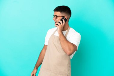 Restoran garsonu mavi arka planda biriyle cep telefonuyla sohbet ediyor.