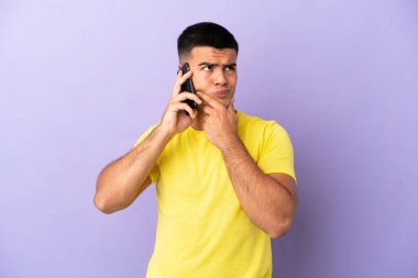 İzole edilmiş mor arka planda cep telefonu kullanan genç yakışıklı adamın şüpheleri var.
