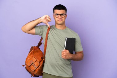 Tecrit edilmiş arka planda yakışıklı bir öğrenci, olumsuz ifadeyle baş parmağını aşağı gösteriyor.