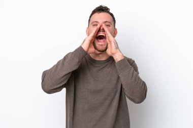 Genç Brezilyalı adam beyaz arka planda izole edilmiş bağırıyor ve bir şey duyuruyor.