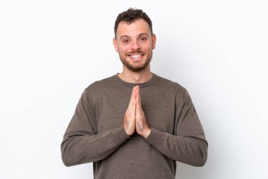 Beyaz arka planda izole edilmiş genç Brezilyalı adam avuç içlerini bir arada tutuyor. İnsan bir şey ister.