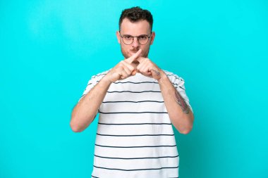 Mavi arka planda izole edilmiş genç Brezilyalı bir adam sessizlik işareti gösteriyor.