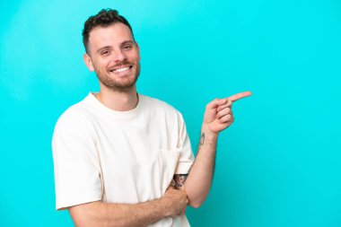 Mavi arka planda izole edilmiş genç Brezilyalı adam parmağını yana doğru gösteriyor.