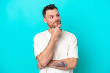 Genç Brezilyalı bir adam mavi arka planda izole edilmiş bir şekilde yukarı bakarken bir fikir düşünüyor.