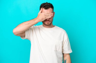 Genç Brezilyalı adam mavi arka planda tek başına, gözleri elle kapatıyor. Bir şey görmek istemiyorum.