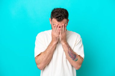 Genç Brezilyalı adam mavi arka planda izole edilmiş, yorgun ve hasta bir ifadeyle.