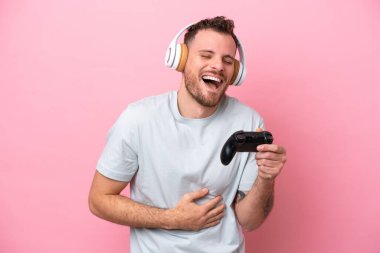 Pembe arka planda izole edilmiş bilgisayar oyunu kontrolörüyle oynayan Brezilyalı genç adam çok gülümsüyor.