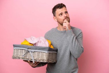 Genç Brezilyalı bir adam pembe arka planda izole edilmiş bir çamaşır sepeti tutuyor. Şüpheleri var.