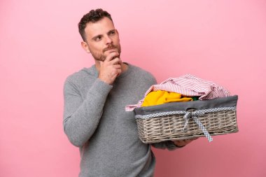 Genç Brezilyalı bir adam pembe arka planda izole edilmiş bir çamaşır sepeti tutuyor ve yukarı bakıyor.