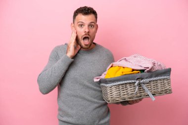 Genç Brezilyalı bir adam pembe arka planda izole edilmiş bir çamaşır sepeti tutuyor. Şaşırmış ve şok olmuş bir yüz ifadesi var.