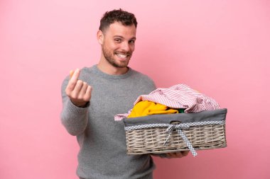 Genç Brezilyalı bir adam pembe arka planda izole edilmiş bir çamaşır sepeti tutuyor ve para hareketi yapıyor.