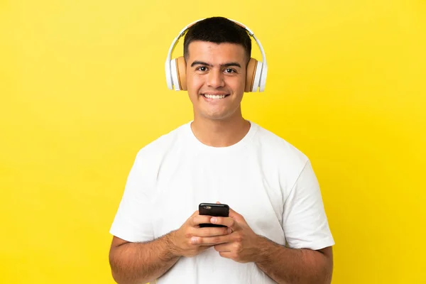 Молодой Красивый Мужчина Изолированном Желтом Фоне Слушает Музыку Мобильным Телефоном — стоковое фото